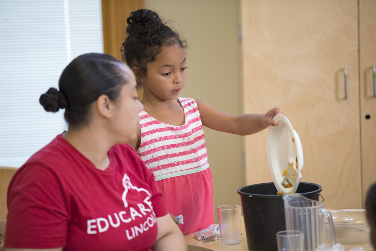 teacher and girl pouring uneaten food into bowl